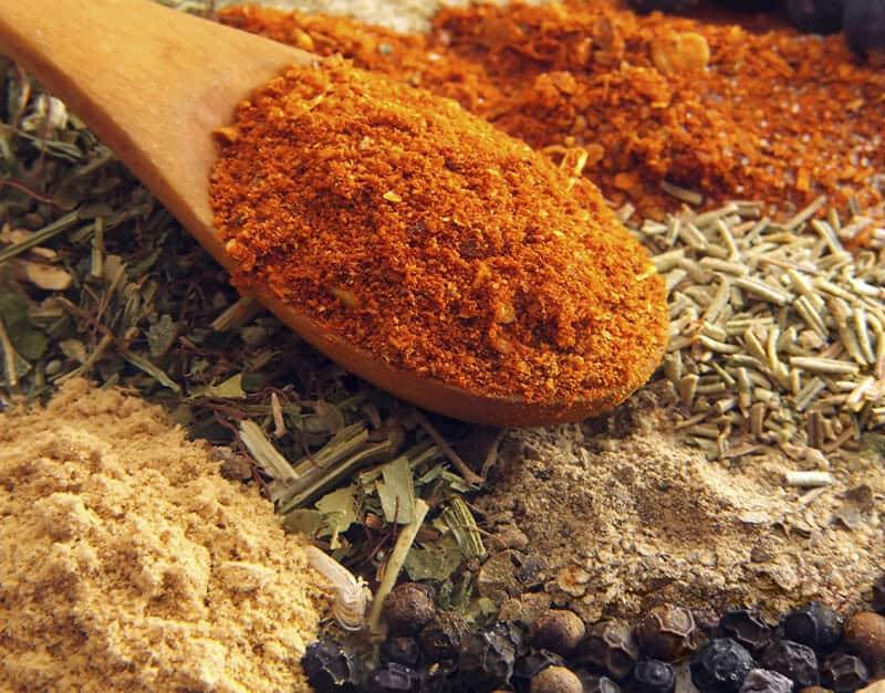 Sausage seasoning blend with a wooden spoon holding red chili powder.