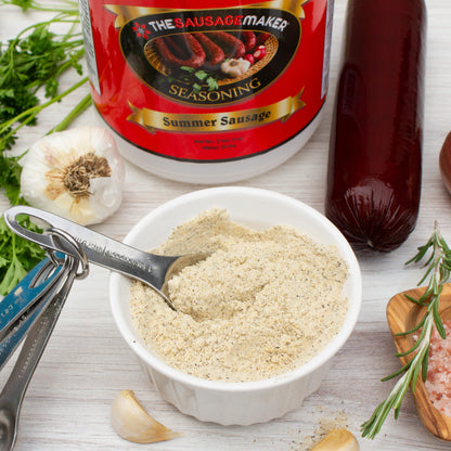 Bowl of summer sausage seasoning with a spoon, surrounded by ingredients on a wooden surface.