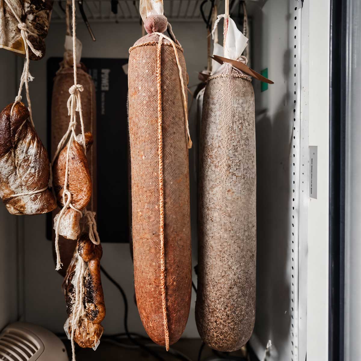 Black pepper and hot pepper spice lined sausages hanging in a dry curing chamber.