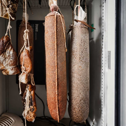 Black pepper and hot pepper spice lined sausages hanging in a dry curing chamber.