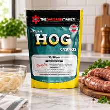 A bag of Natural Hog Casings stands on a wooden table in a kitchen setting, with cooked sausages nearby.