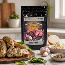 A pouch of The Sausage Maker Spinach Feta Chicken Seasoning stands on a kitchen counter with cooked sausage slices, onion, garlic, basil, and small bowls of ingredients around it.